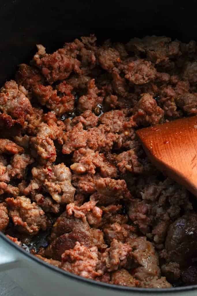 Italian sausage browning in a pot with a wooden spoon for making tortellini soup.